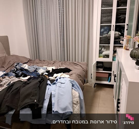 בגדים מסודרים על מיטה וארון פתוח עם בגדים מקופלים